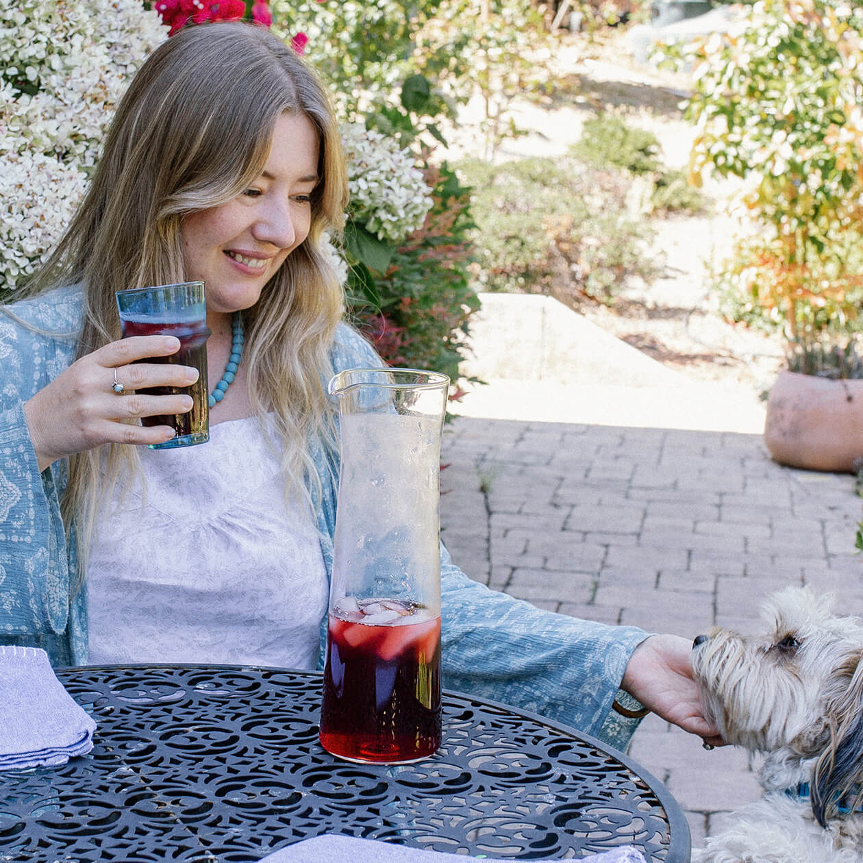 A young woman enjoys a herbal iced tea outdoors with her dog