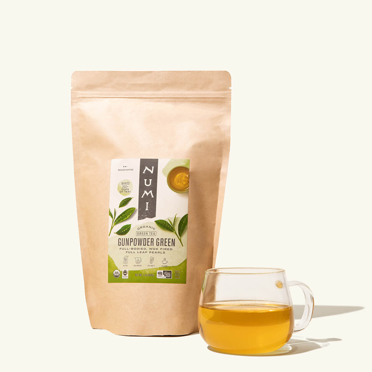 A bag of loose leaf Numi Gunpowder Green tea with a cup of brewed tea in a clear cup
