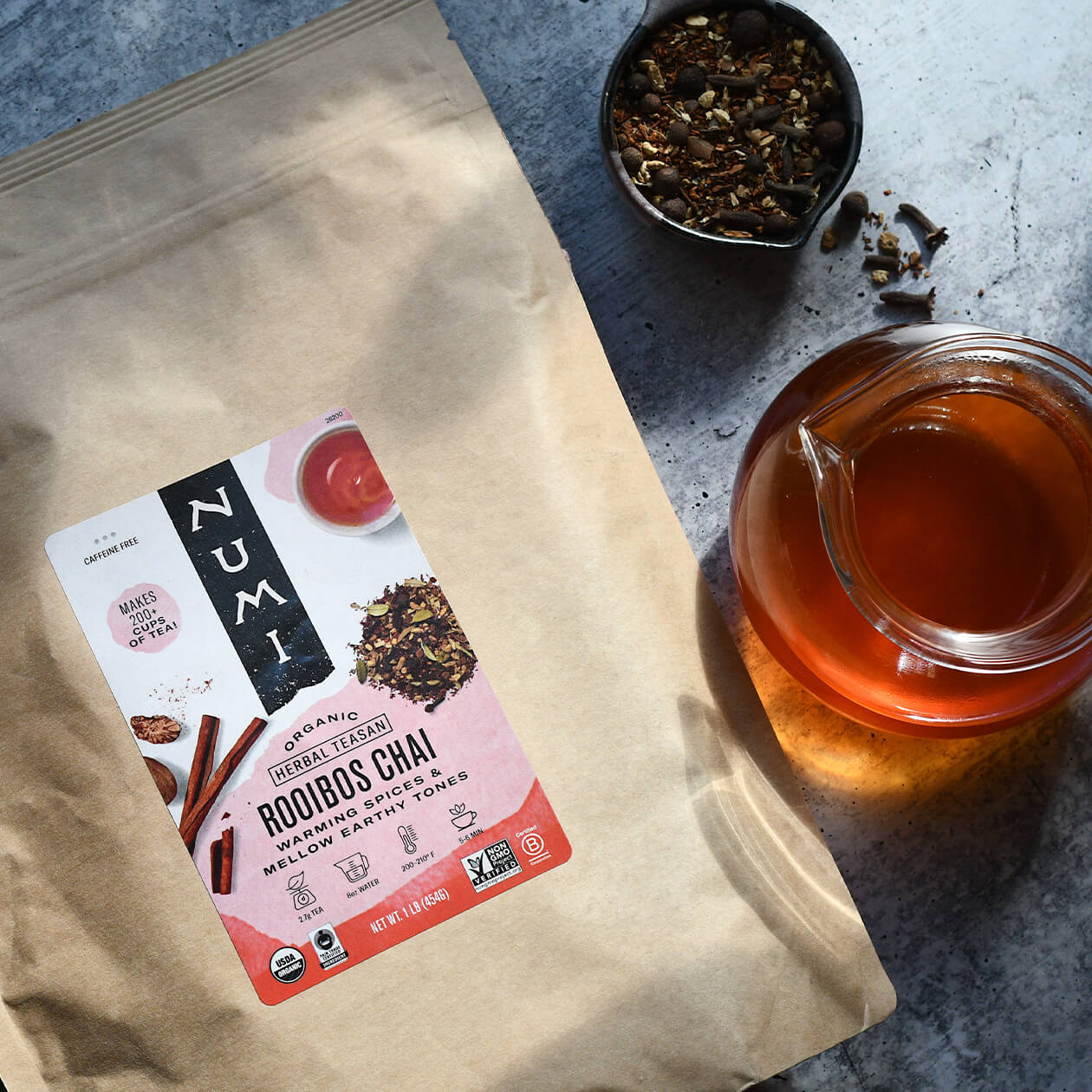 A bag of loose leaf Rooibos Chai tea next to the loose tea and a brewed pot of tea