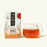 A box of Numi's Rooibos next to a brewed cup of tea in a clear cup