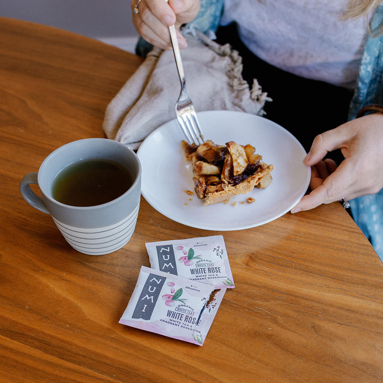 A person enjoying a cup of Numi White Rose Tea with dessert