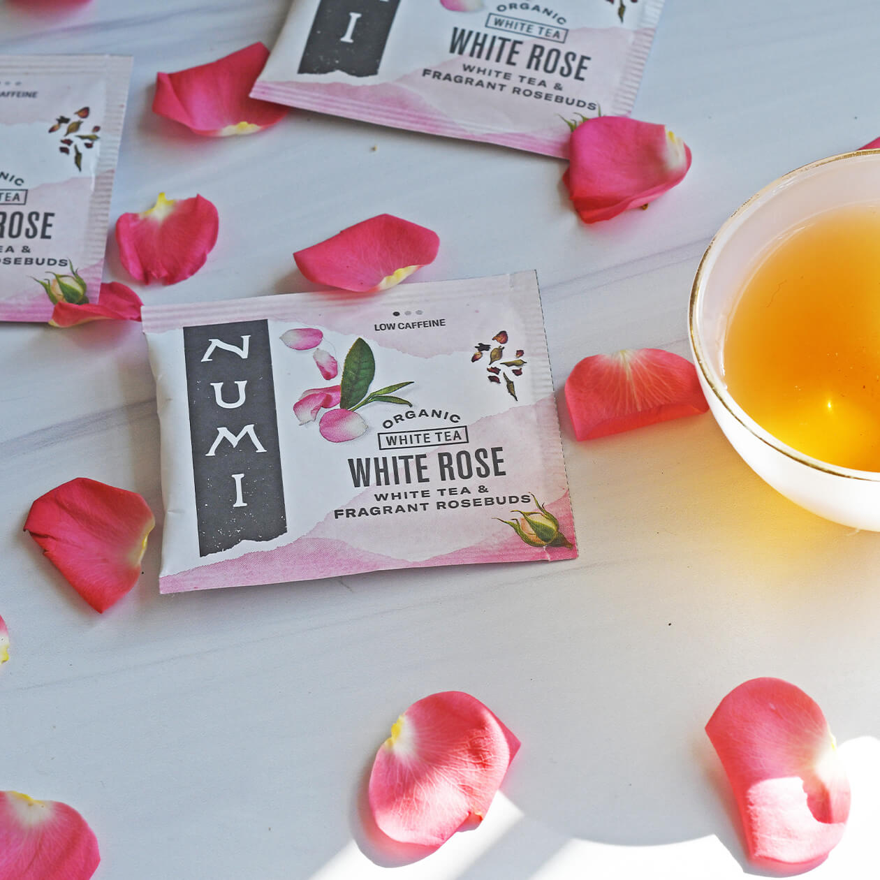 Numi White Rose tea bags with rose petals and a brewed cup of tea on a countertop