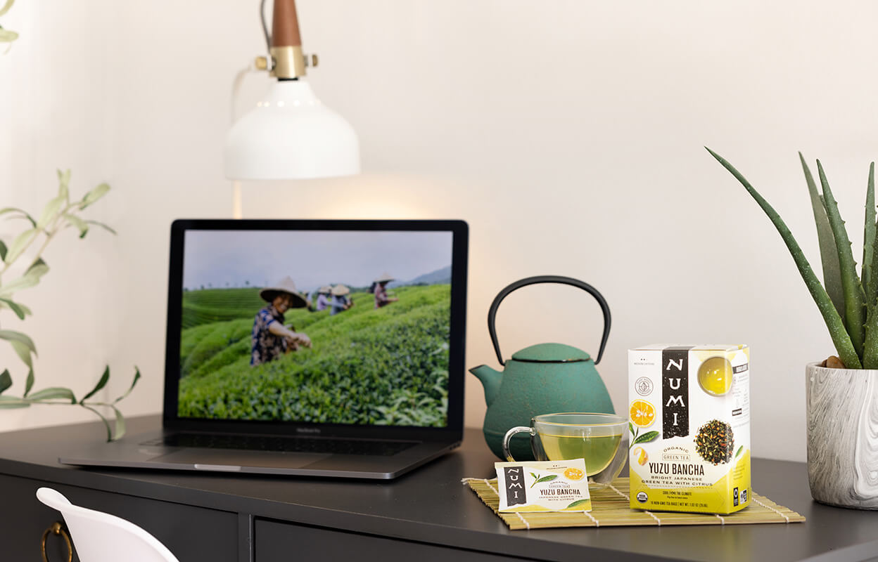A cup of Numi Organic Yuzu Bancha tea next to a laptop on a desk