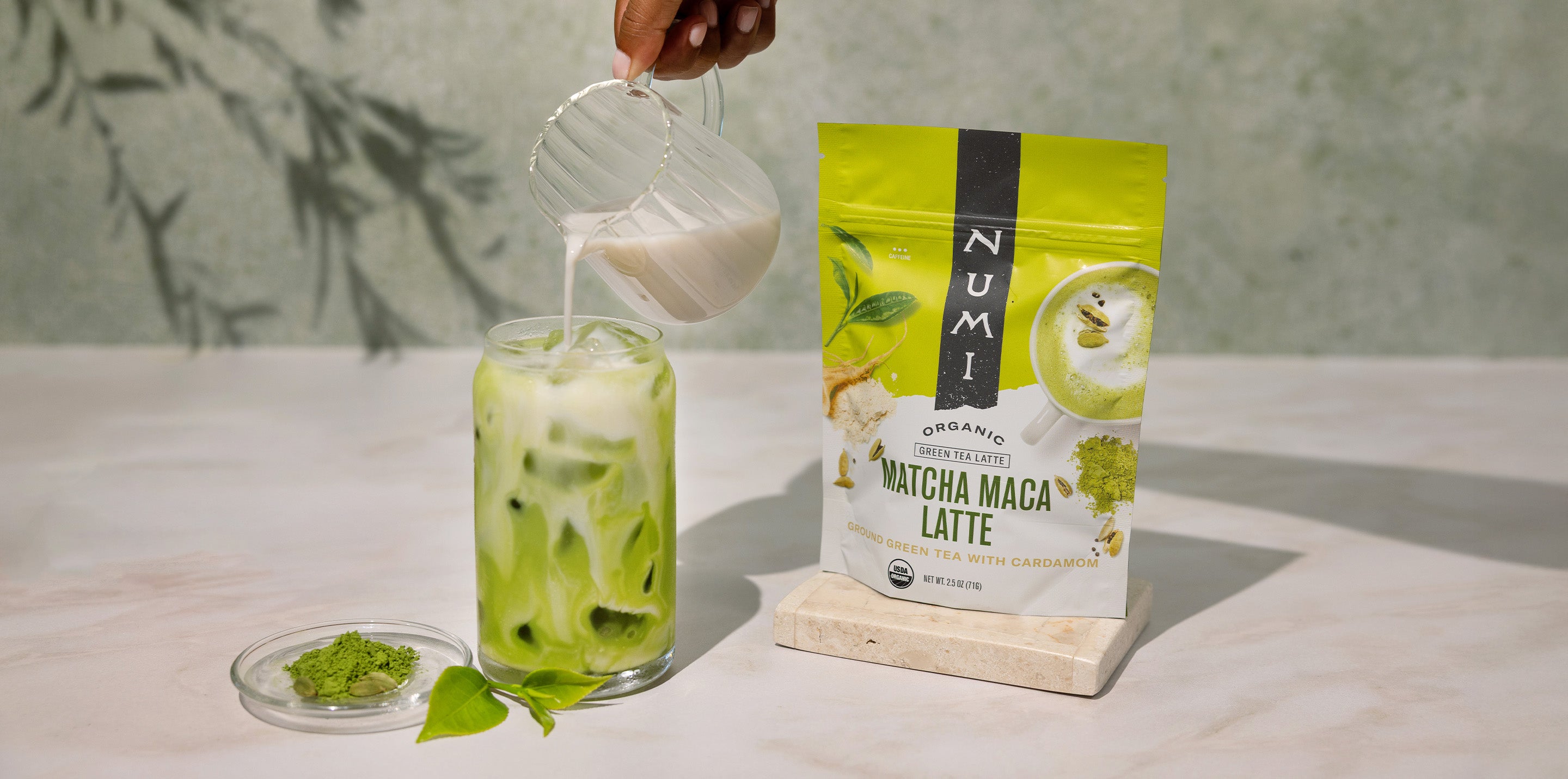 Iced matcha latte with Numi Matcha Maca Latte packaging on a light surface.
