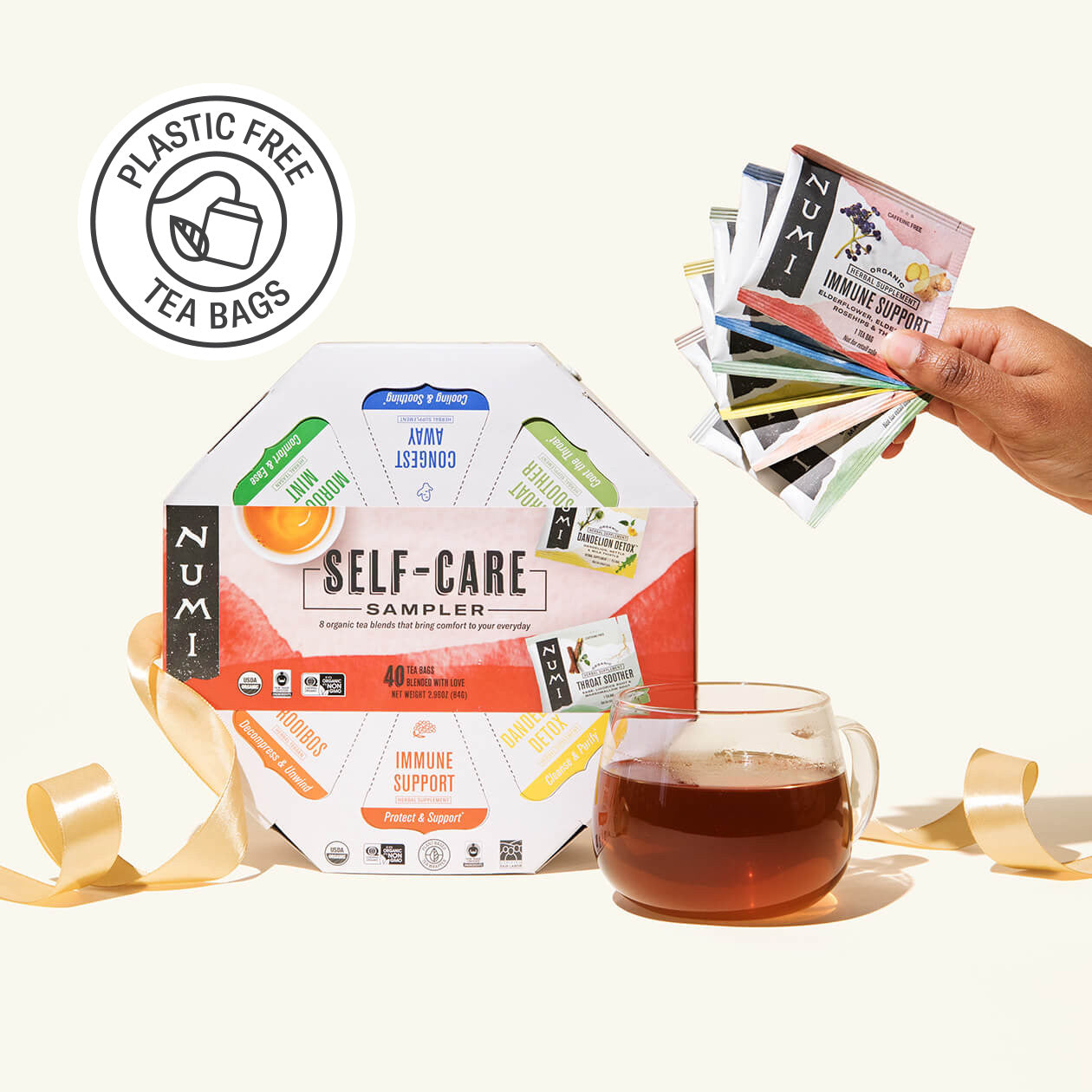 Numi tea sampler pack with a glass of tea and plastic-free tea bags label on a white background