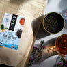 A bag of Numi Aged Earl Grey tea in the sunlight with a cup of brewed loose leaf tea