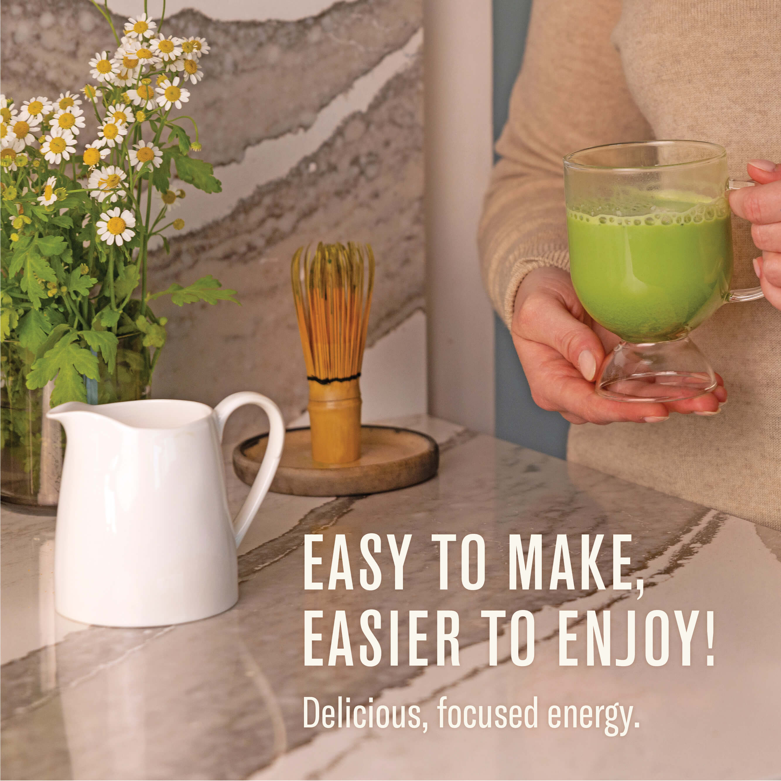 Person holding a glass of green drink with a pitcher and flowers on a table, text 'Easy to make, easier to enjoy! Delicious, focused energy.'.
