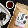 A bag of organic Numi Chinese Breakfast tea next to a pile of loose leaf tea and a brewed cup