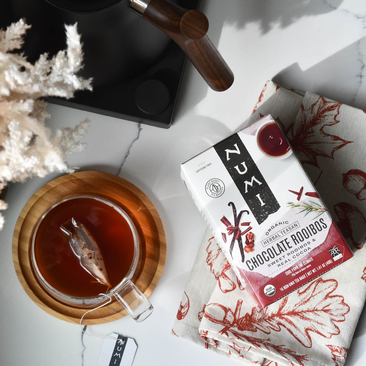 A box of Numi Chocolate Rooibos on a countertop with a tea kettle and cup of brewed tea