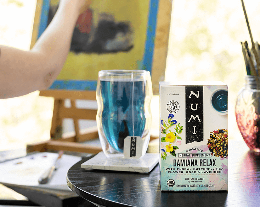 A person painting in their studio enjoys a cup of Numi's Damiana Relax tea