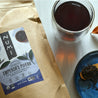 A bag of Numi's organic Emperor's Puerh with loose tea and a brewed cup on a table