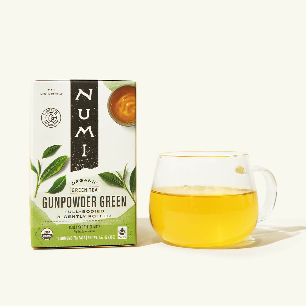 A box of Numi's Gunpowder Green next to a brewed cup of tea in a clear cup