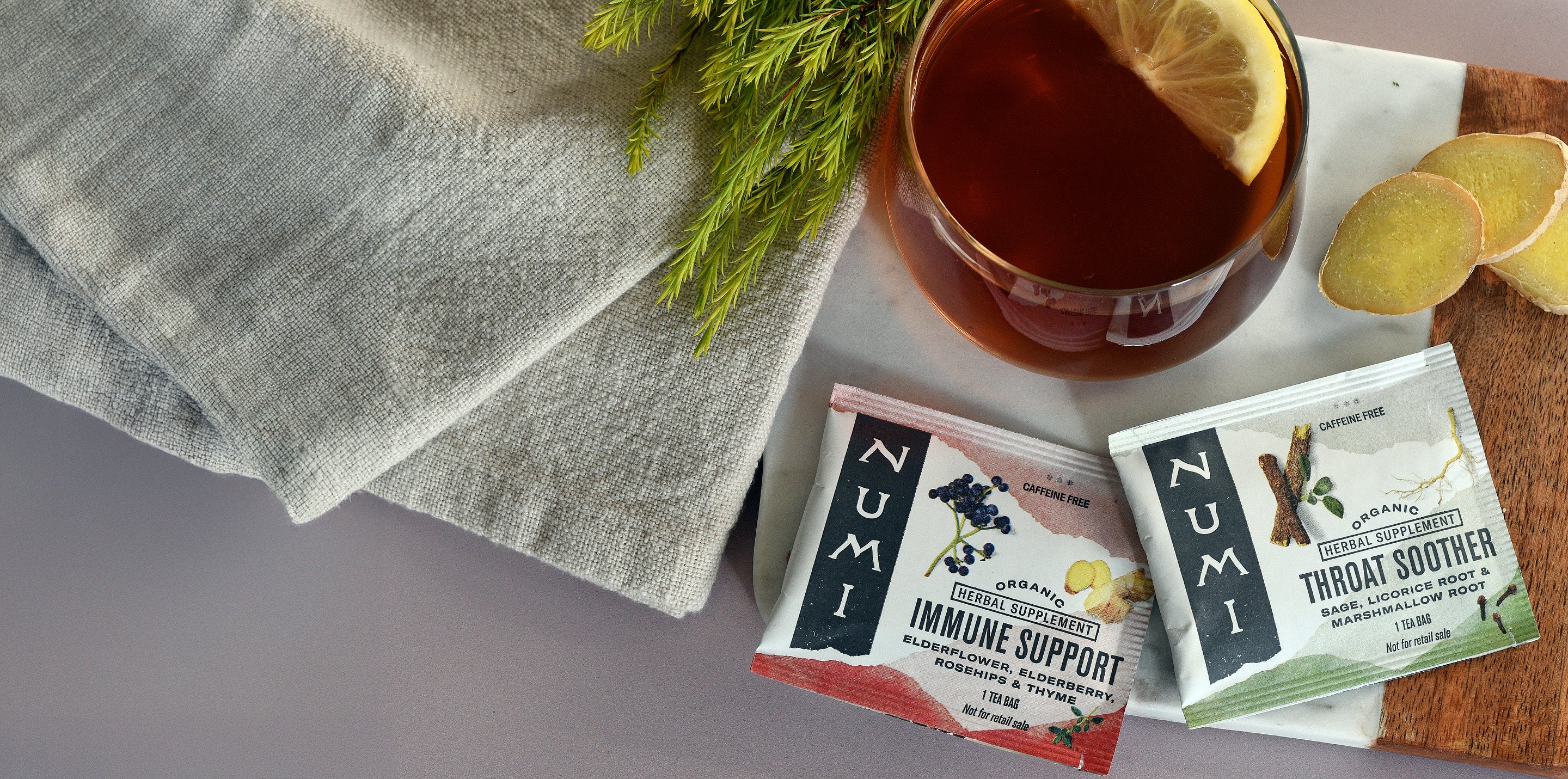 Numi tea bags with a glass of tea and lemon slices on a wooden board.