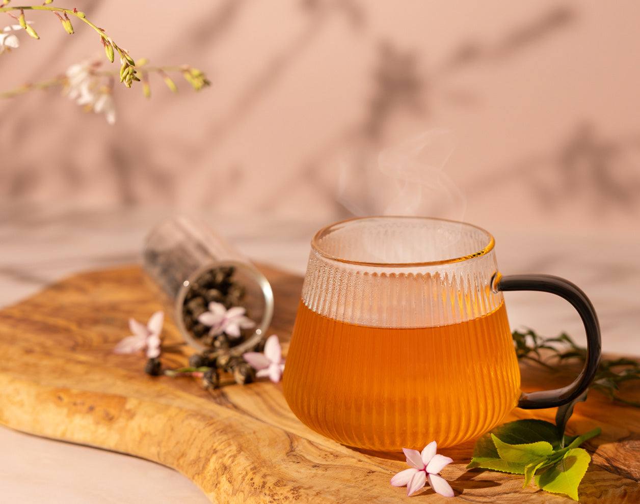 Glass mug with jasmine green tea on a wooden board with flowers and leaves.