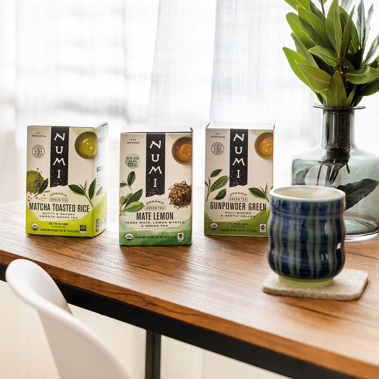 A trio of Numi green tea boxes on a desk with a brewed hot cup of tea