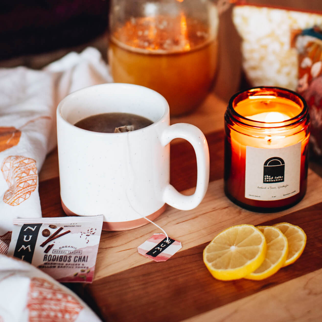 A cup of hot Rooibos Chai brewing on a table with lemon slices and a candle