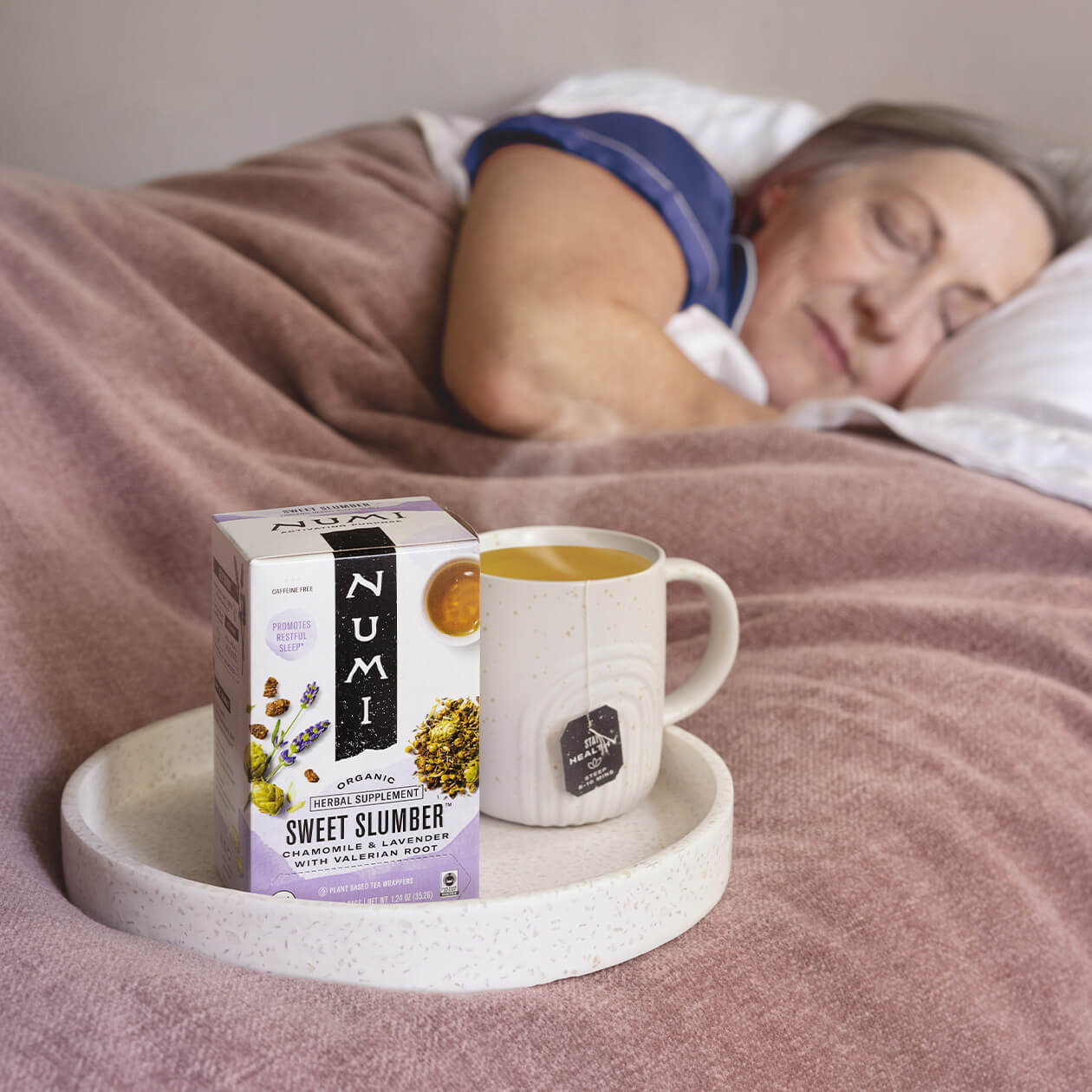 A woman sleeping in her bed next to a cup of Sweet Slumber tea
