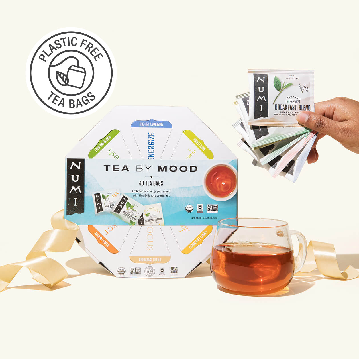 Numi tea by mood packaging with a hand holding tea bags and a cup of tea on a white background.